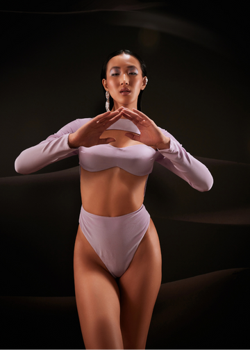 Woman in a light purple bodysuit standing against a dark background