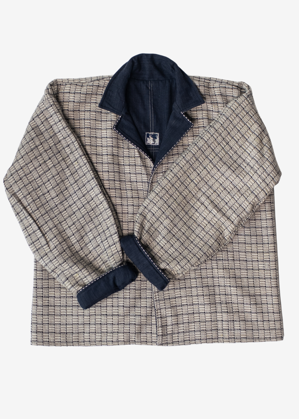 A men's long-sleeve plaid overshirt jacket in beige and navy blue, featuring a solid navy blue collar and cuff trim, laid flat against a light gray background.