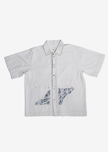 A short-sleeve button-up shirt in light gray fabric, featuring two front patch pockets with a blue-gray fish pattern and a central decorative stitched detail.