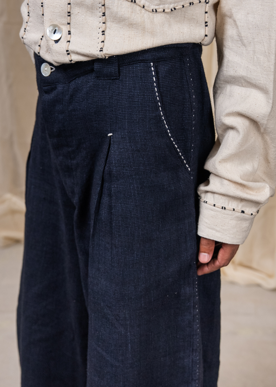 Close-up of a person wearing dark navy wide-leg trousers with visible white contrast stitching and a cream-colored embroidered top.