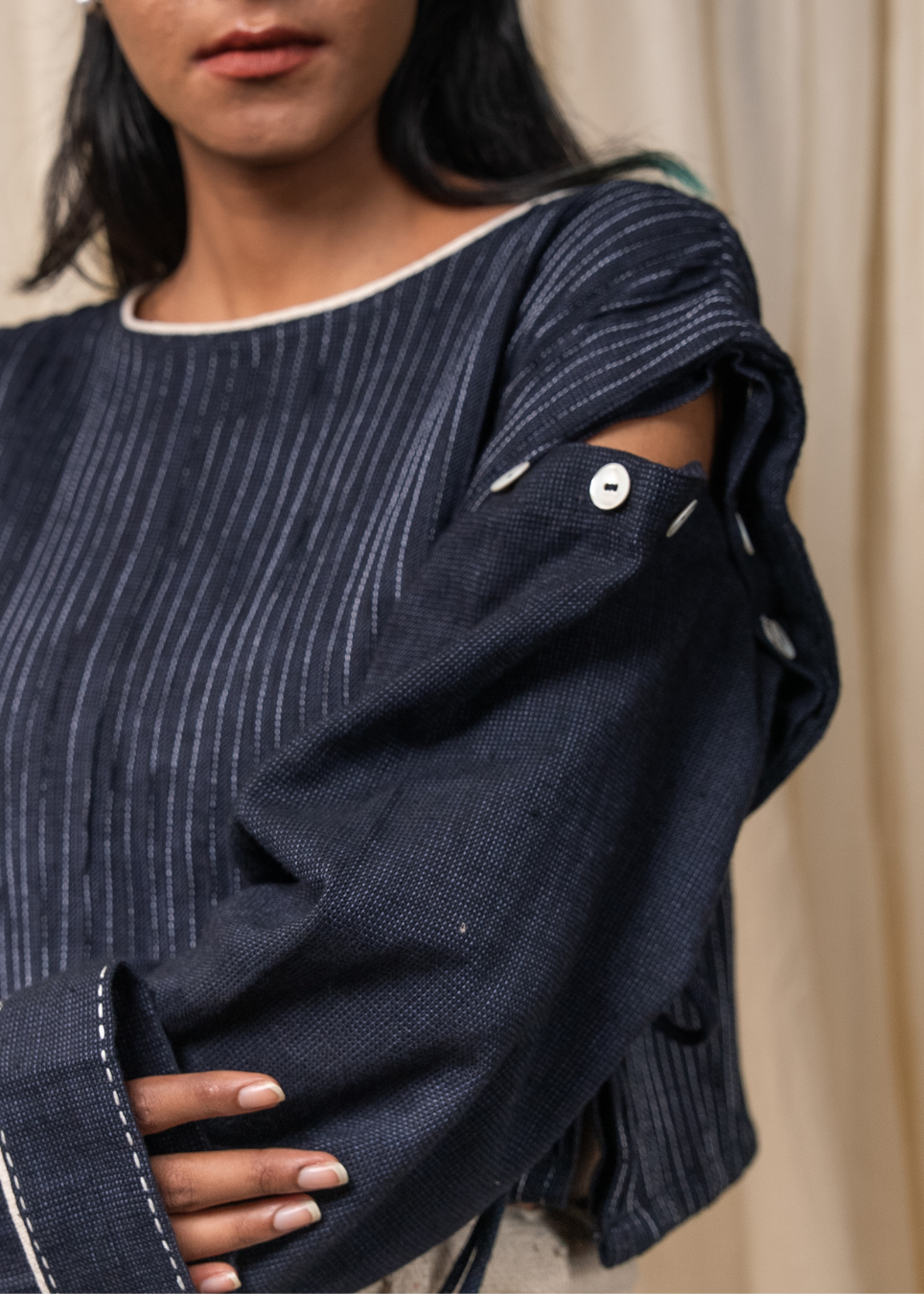 Close-up of a person wearing a dark navy textured top with thin white vertical stripes, featuring a cutout shoulder and white contrast stitching.