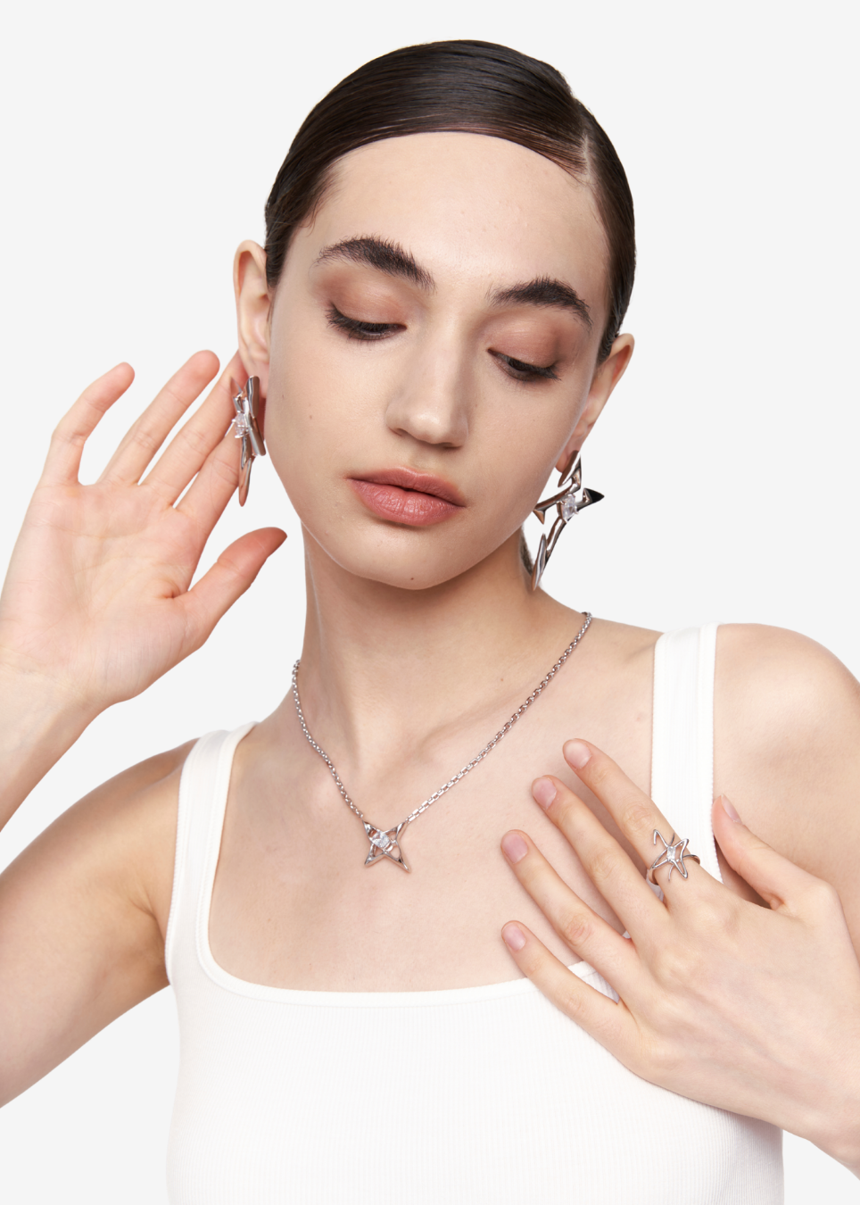 A model wearing a silver geometric star pendant necklace, matching star earrings, and a star ring, styled with a white top against a light gray background.