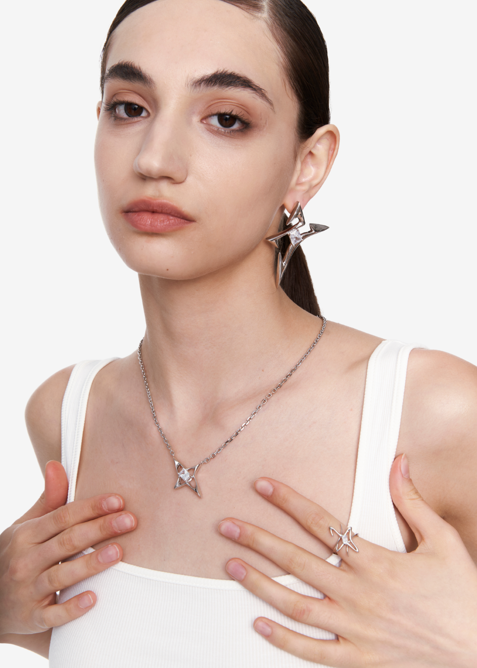 A model wearing a silver star-shaped pendant necklace, matching star earrings, and a star ring, styled with a white ribbed tank top against a clean white background.