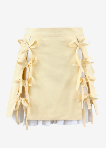A pale yellow mini skirt with side tie-front details and layered ruffle trim, shown against a plain light gray background.